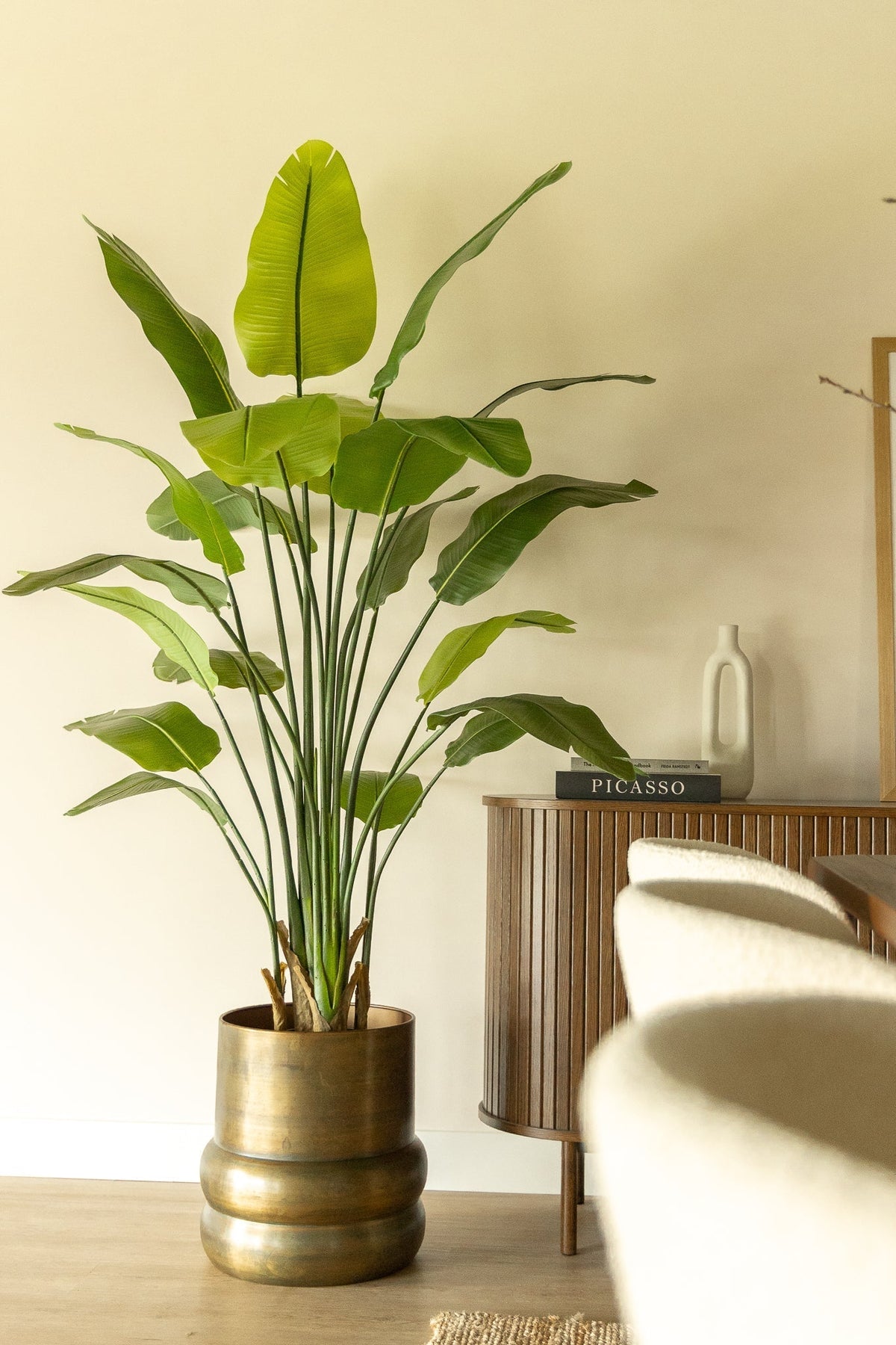 Kunstpflanze Strelitzia in einem messingfarbenen Topf in einem hellen Wohnzimmer
